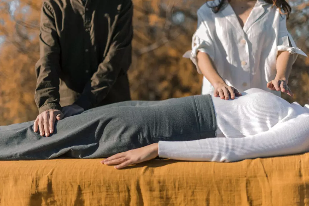 Dos personas realizando una terapia de Reiki sobre una chica tumbada.