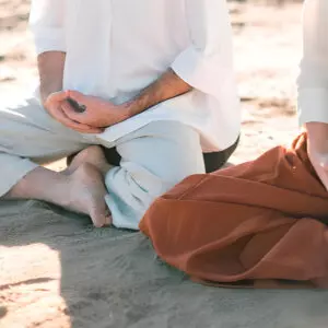 Dos personas practicando meditación en la playa.