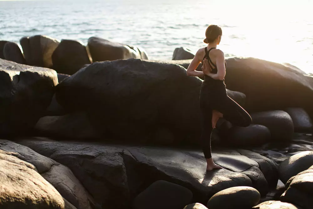 Chica sobre unas rocas al lado del mar, practicando yoga y Qi gong.