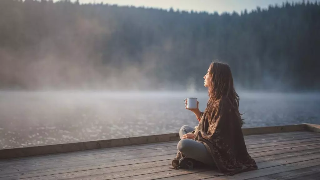 Mujer relajada disfrutando de una taza de té junto al lago